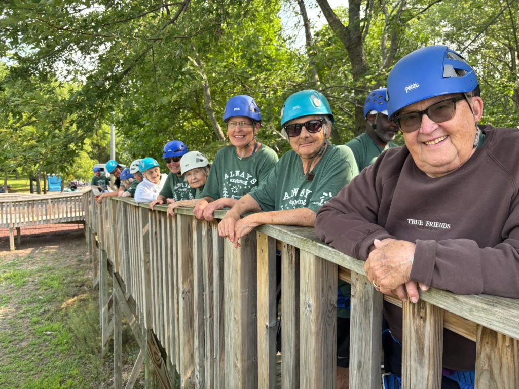 Camp Joy participants gather on a wooden platform while waiting for their turn on the accessible zipline.